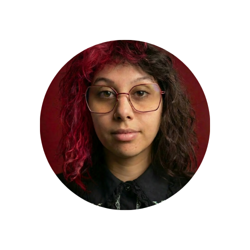 Icona tonda con Chiara in primo piano. Ha capelli ricci rossi e neri ed occhiali esagonali rossi